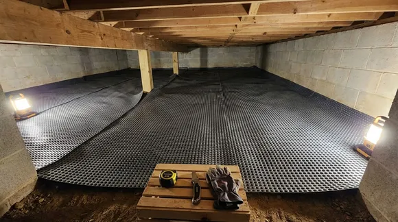 Black dimpled drainage matting laid across a crawlspace floor before the liner goes down